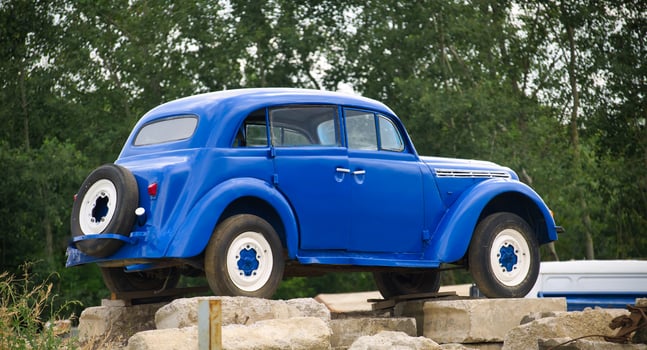 Classic blue vintage car parked outdoors on rocky terrain with green trees in the background photo