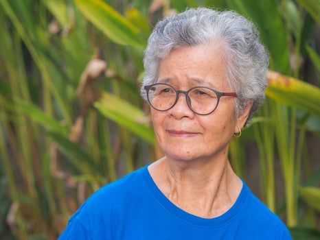 Cheerful senior woman with short gray hair wearing glasses, smiling and looking away while standing in a garden. Space for text. Concept of aged people and healthcare photo