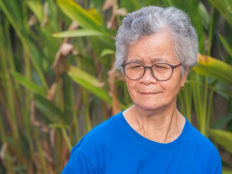 Portrait of a senior woman with short gray hair wearing glasses and looking down while standing in a garden. Space for text. Concept of aged people and healthcare photo
