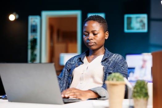 Focused college student working on her thesis, using a laptop for researching, and reviewing information online. Dedicated and determined, black woman working from home on personal computer. photo