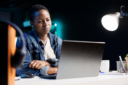 Tired African American college student at desk with a laptop, stressed and overwhelmed by projects and studies. Young black woman feeling unwell is looking at and reading emails on wireless computer. photo