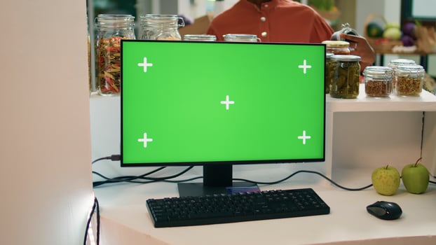 Seller at register uses greenscreen on computer, showing isolated copyspace display on pc monitor. Young man small business owner encourages healthy lifestyle with blank chromakey. photo