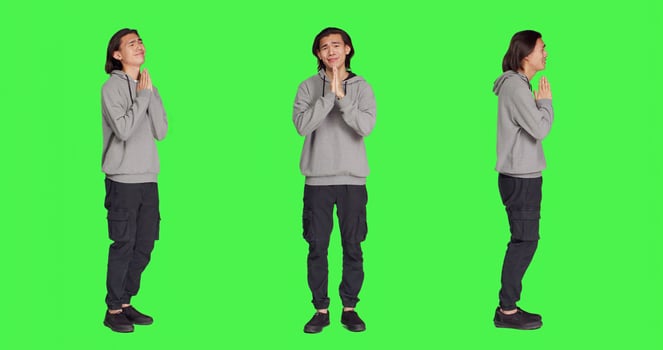 Male model praying to God on camera and doing prayer hands sign, standing over full body greenscreen. Young man feeling hopeful and having belief in Jesus, religion symbol. photo