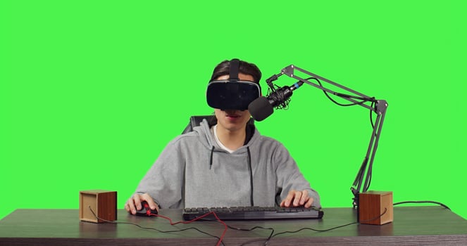 blogger recording live gameplay at desk, playing online tournament with virtual reality interactive headset. Asian man streaming videogames vlog, content creator on greenscreen. photo