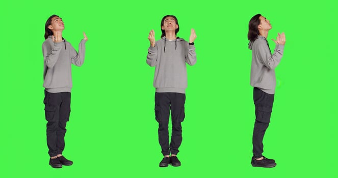 Young adult praying and hoping for luck, talking to Jesus and having belief in bigger entity. Asian person being spiritual and religious over isolated full body greenscreen. photo