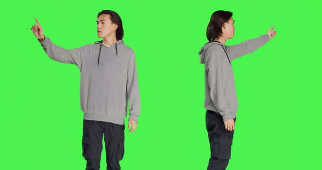 Person indicating left or right directions on camera, pointing to both sides and recommending another path. Asian young man advising someone to go that way, greenscreen backdrop. photo
