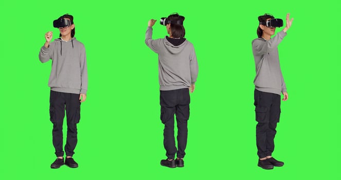 Young adult enjoys virtual reality gadget in studio with greenscreen background, using interactive vision or simulation on headset. Modern guy having fun with artificial intelligence vr glasses. photo