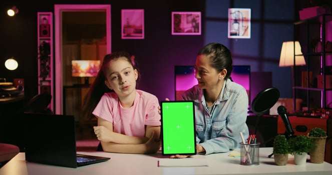 Child and parent in home studio film together for social media, holding isolated screen laptop on desk promoting sponsor. Mom and her young kid recording content next to chroma key notebook photo