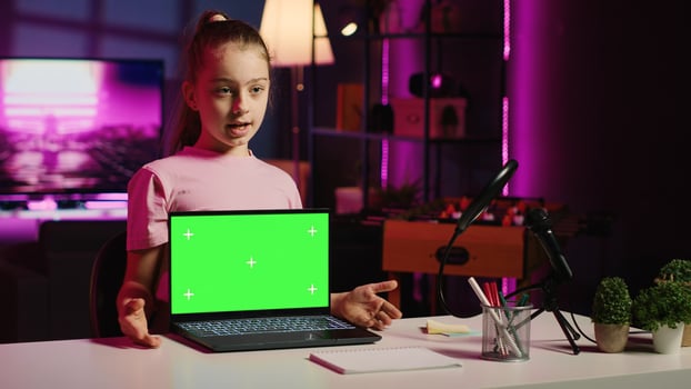 Kid influencer in home studio using recording gear to record review of mockup laptop. Young girl online show host filming electronics haul, presenting isolated screen notebook for viewers photo