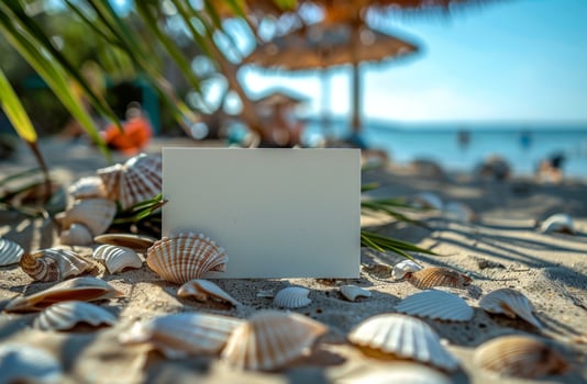 Blank card on a sandy beach with seashells, palm leaves, and ocean in the background, tropical vibe photo