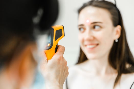 Smiling Woman Undergoing Infrared Temperature Check by Healthcare Professional photo