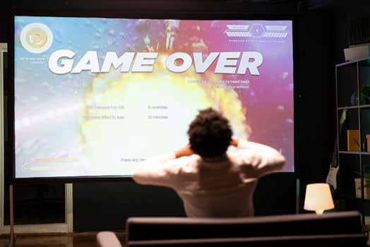Gamer upset at seeing game over message on ultrawide TV screen playing arcade space shooter videogame. Man spending time at home on gaming system, frustrated after losing online competition photo