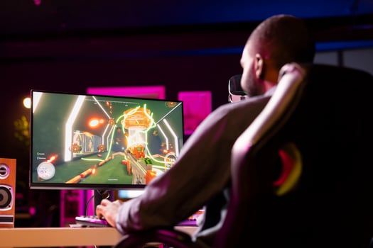 Man in neon lit apartment playing immersive games on gaming PC at computer desk, unwinding after work. Gamer competing against enemies in internet multiplayer shooter photo