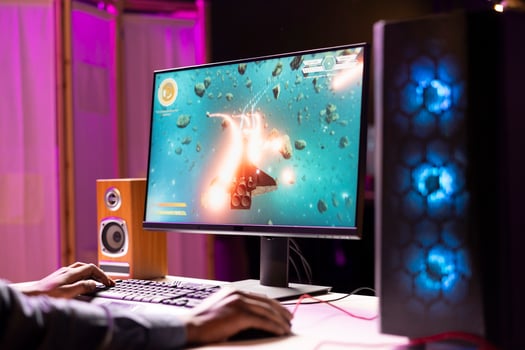 African american man playing SF space videogame on PC screen, shooting asteroids. Gamer enjoying spaceship flying game on computer desktop display, navigating through meteorites photo
