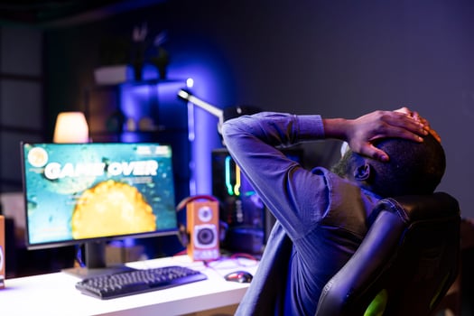 Depressed gamer upset after losing in online multiplayer videogame, being defeated by other players. African american man putting hands on head in frustration after seeing game over screen photo