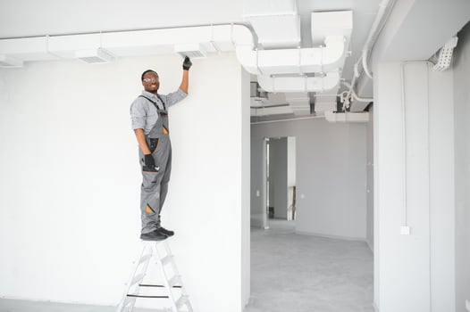 Industrial Theme. Warehouse Heating and Cooling System Installation by Professional Caucasian Technician. Commercial Building Ventilation Rectangle Canals. Air Distribution photo
