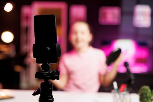 Close up shot of professional recording smartphone camera used by gen Z internet star to do livestream. Focus on production gear used by cute kid in blurry background to do live broadcast photo