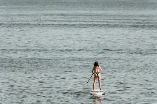 Sea woman sup. Silhouette of happy positive young woman in bikini, surfing on SUP board, confident paddling through water surface. Idyllic sunset. Active lifestyle at sea or river. Slow motion. photo