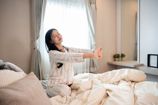A woman in pajamas is keeping her eyes closed and stretching her arms on the bed after waking up. photo