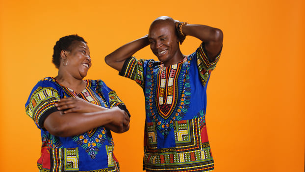 Cheerful husband and wife laughing together on camera, having fun with silly jokes over orange background. African american couple enjoying funny moments, carefree people laugh. photo