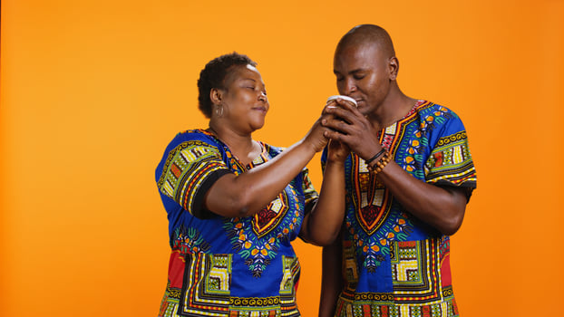 African american couple enjoying smell on fresh coffee, woman holding paper cup and smelling caffeine aroma from hot drink. Ethnic people loving the scent of energy refreshment in studio. photo