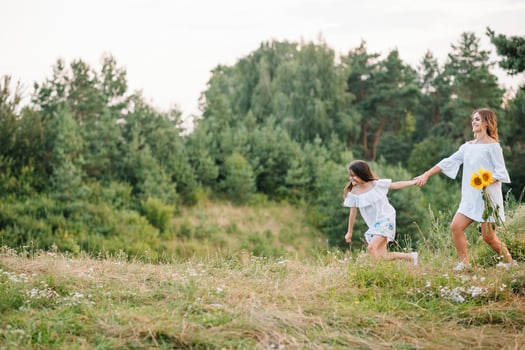 Cheerful mother and her little daughter having fun together in the summer background. Happy family in the nature background. Cute girls with colorful flowers photo