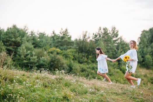 Cheerful mother and her little daughter having fun together in the summer background. Happy family in the nature background. Cute girls with colorful flowers photo