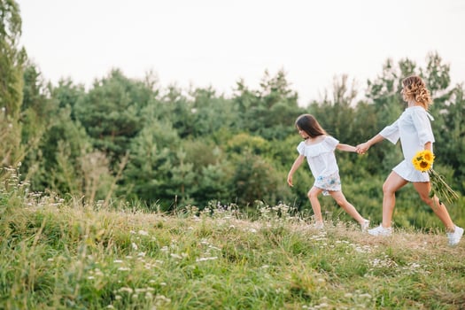 Cheerful mother and her little daughter having fun together in the summer background. Happy family in the nature background. Cute girls with colorful flowers photo