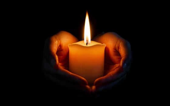 holding a burning candle in his hands on a black background photo