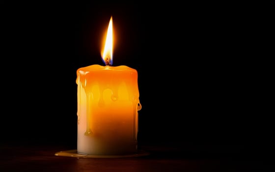 yellow burning candle with dripping wax on wooden table photo