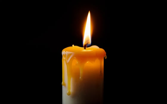 yellow burning candle with dripping wax close-up photo