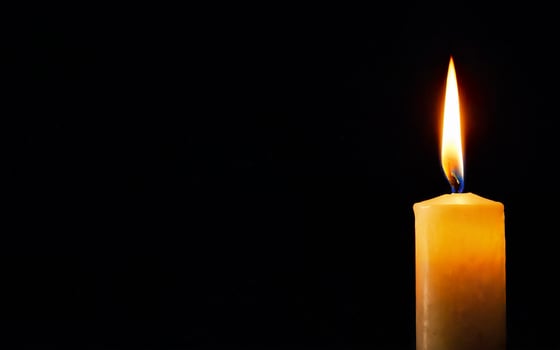 one burning candle on a black background with space for text close-up photo