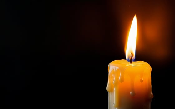 burning candle with dripping wax close-up on a black background with space for text photo