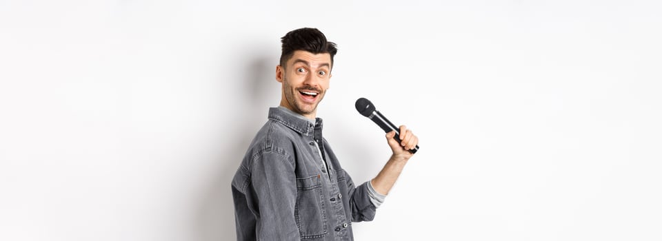 Profile of handsome smiling man holding mic, turn head at camera with excited face, singing karaoke and perform standup, standing on white background photo
