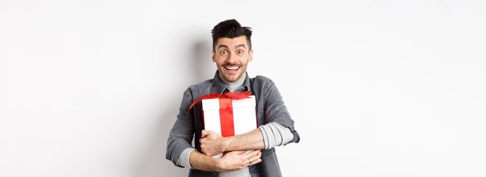 Happy caucasian man holding surprise gift, hugging present and smiling thankful, looking at camera with love and appreciation, celebrate valentines holiday, white background photo