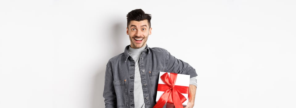 Happy Valentines day. Surprised and happy guy holding gift box and look at camera, smiling amazed, celebrating holiday, bring present on romantic date, white background photo