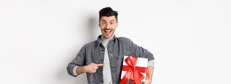 Happy Valentines day. Excited caucasian guy pointing at gift box from lover, smiling and looking amazed, buying presents on romantic date, white background photo