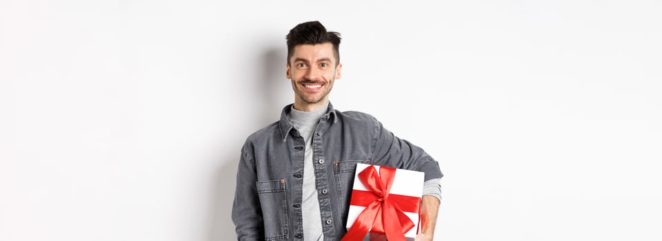 Happy Valentines day. Smiling handsome man bring gift on romantic date, holding box with present and looking romantic at camera, white background photo