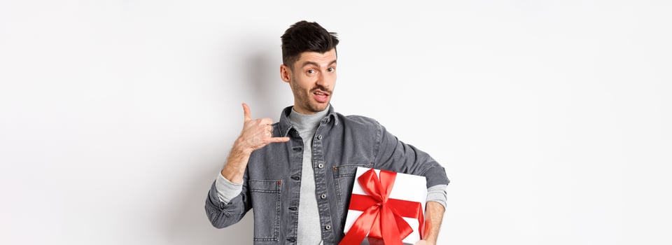 Macho guy with gift box show call me phone gesture, flirting with you, standing boastful on white background. Relationship and Valentines day concept photo