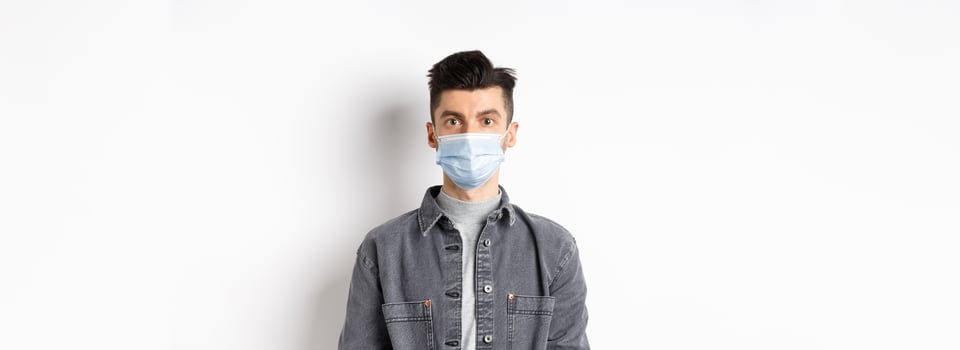 Health, covid and pandemic concept. Handsome young man in medical mask from coronavirus, use preventive measures during virus outbreak, standing on white background photo
