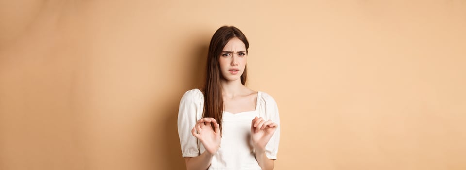 Stay away from me. Disgusted young woman frowning and looking with aversion at something stinky, rejecting disgusting thing, standing on beige background photo