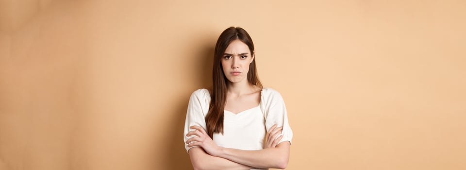 Angry girlfriend cross arms on chest and frowning, looking offended or disappointed, sulking at you, standing mad on beige background photo