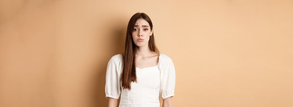 Please I want it. Silly woman make cute sad eyes and begging to buy her something, standing with innocent pleading loo, beige background photo