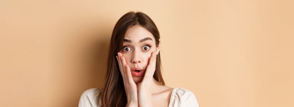 Face of surprised girl saying wow, touching cheeks and staring excited at camera, standing on beige background photo