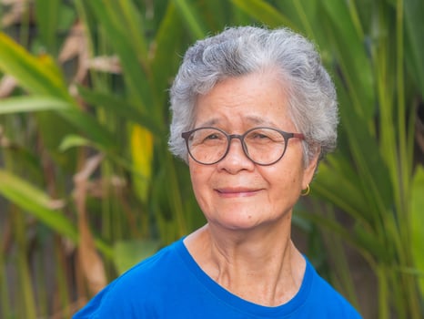 Portrait of a beautiful senior woman with short gray hair wearing glasses, smiling and looking at the camera while standing in a garden. Space for text. Concept of aged people and healthcare photo