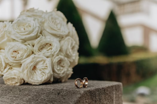 A bouquet of white roses sits on a stone pedestal next to two gold wedding rings. Concept of love and commitment, as the rings symbolize the bond between two people photo