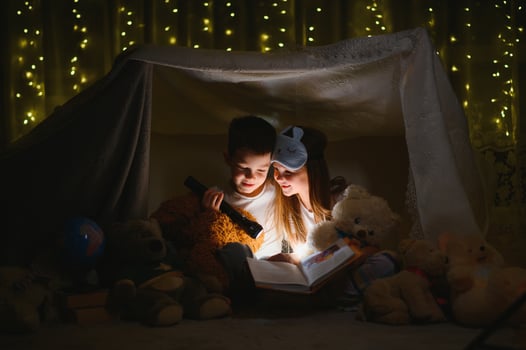 Little kids involving in reading amazing book. They lying in nice toy tent in playroom. Boy holding flashlight in hand photo