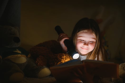 Little girl are reading a book with flashlights in tent. Happy girl playing at home. Funny lovely kid having fun in room. photo