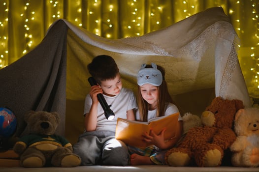 reading and family games in children's tent. boy and girl with book and flashlight before going to bed photo