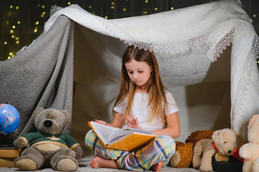 child girl reading with book and flashlight and teddy bear in tent. before going to bed photo
